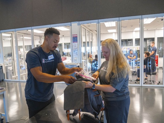A young man stuffs donations into a backpack held by his instructor in a clinical training room.