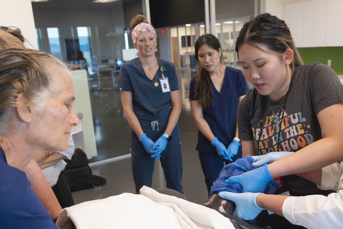 Female medical student working on a simulation patient while classmates look on.